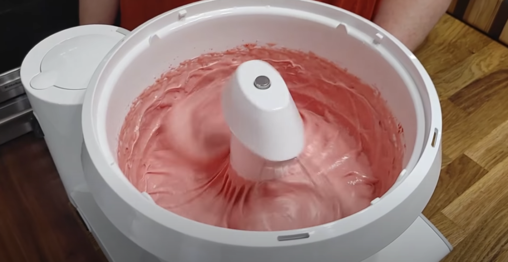 Pink cake batter being mixed in a white stand mixer.