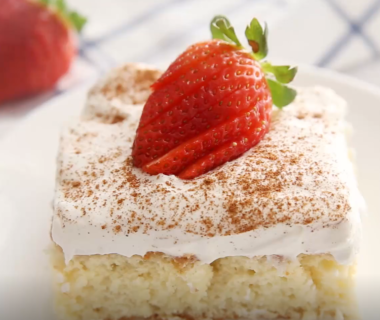 A piece of tres leches cake with cream and a strawberry on top