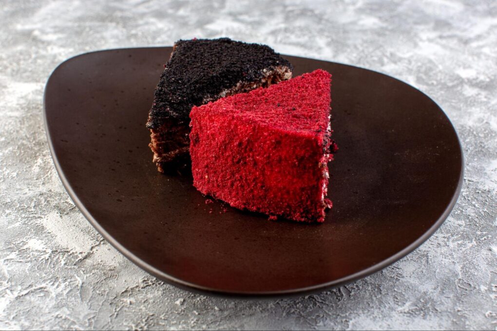 a slice of traditional chocolate cake and a slice of red velvet cake on a dark brown plate and white-gray background