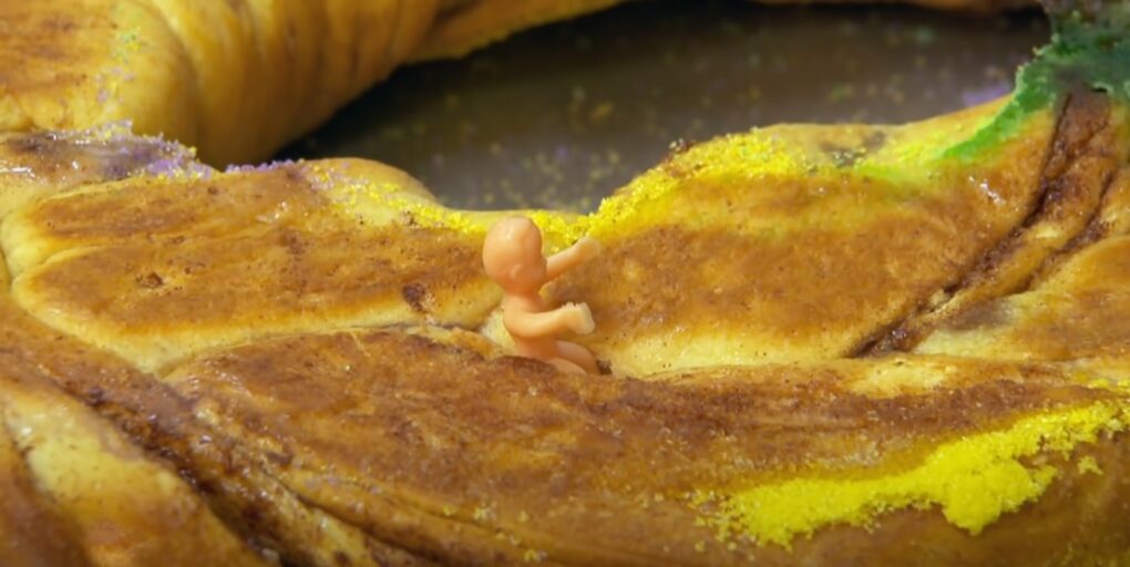 a clow view of a plastic figurine of a baby placed inside king cake's dough