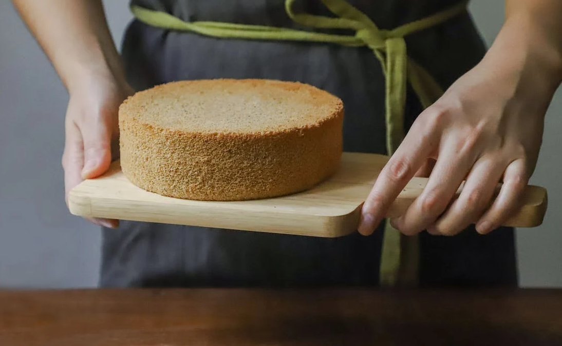 a woman is holding a freshly baked sponge cake in an apron