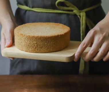 a woman is holding a freshly baked sponge cake in an apron