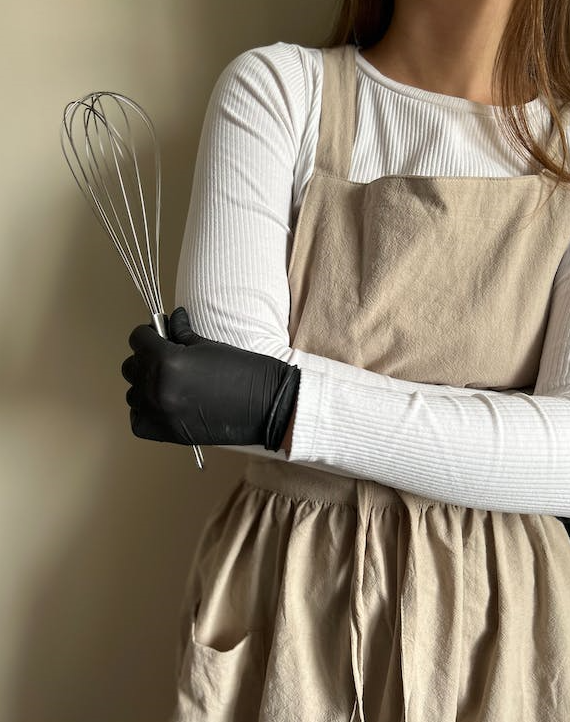 a woman stands with a whisk in an apron